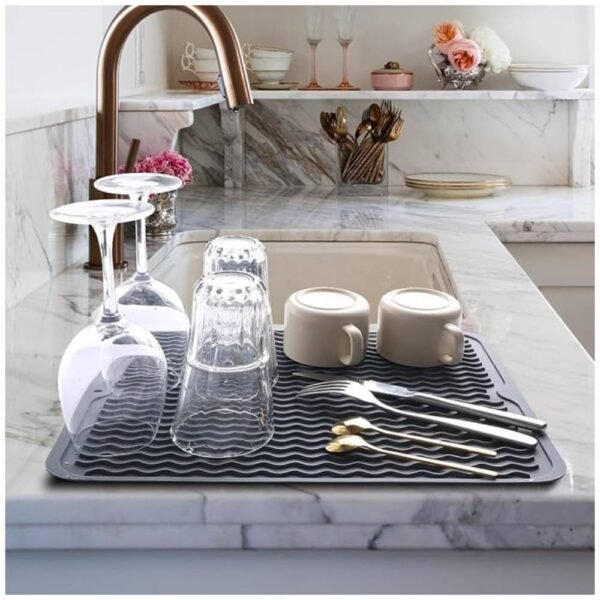 Silicone Dish Drying Mat placed by the sink, holding wet dishes, cups, and utensils with raised ridges for quick drying.