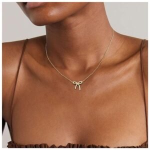 Woman wearing a dainty gold bow necklace, styled as a choker.